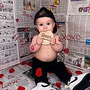 Zeke joined the competition — help win amazing prizes! baby, infant, child, cap, black_pants, white_shoes, newspaper_background, rose_petals, lipstick_marks, wooden_sign, seven_months, sitting, cute, playful, indoor, portrait, love, xoxo, red_hearts, smiling