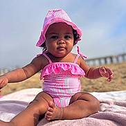 Ari is registered to the contest to win money with this photo: baby, child, swimsuit, pink, hat, beach, towel, sand, sunhat, outdoor, portrait, sitting, infant, cute, summer, person, young_child, sun_protection, relaxing, vacation