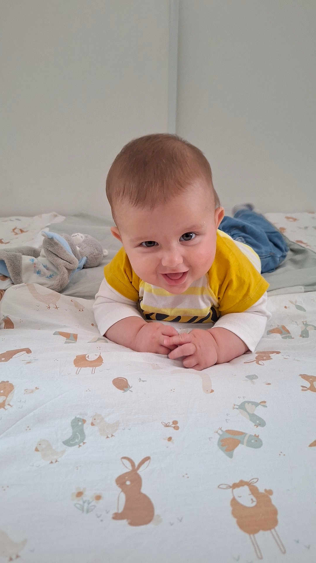 Jules participe au concours pour gagner de l'argent avec cette photo : animal_print, baby, bed, blanket, blue_pants, child, cute, face, hands, home, indoor, infant, lying_down, person, playful, smiling, soft_toy, tongue_out, white_clothing, yellow_clothing