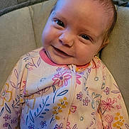 Jensyn is registered to the contest to win money with this photo: baby, child, smile, face, onesie, floral_pattern, pink, pastel_colors, couch, indoor, portrait, infant, cute, happy, young_child, seated, closeup, person, cozy, soft_fabric