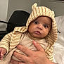 baby, child, hoodie, striped_clothing, hand, indoor, poster, car, curious, wide_eyes, person, seated, blanket, knitwear, adult_hand, cozy, cute, portrait, expression, warm