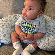 Julian is registered to the contest to win money with this photo: baby, child, infant, sitting, couch, pillow, animal_pattern, curly_hair, socks, shirt, bracelet, red_string, expression, wide_eyes, indoors, cozy, hands, clothing, cute, portrait