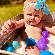 Anslie joined the competition — help win amazing prizes! baby, child, bow, headband, metal_tub, milk, plastic_eggs, purple_eggs, blue_eggs, outdoor, grass, sunlight, skin, water, summer, cute, person, infant, playful, curious