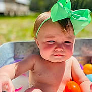 Loralie is registered to the contest to win money with this photo: baby, child, green_bow, plastic_balls, outdoor, sunlight, tub, water, play, summer, cute, headband, skin, happy, fun, colorful, toy, person, young, expression