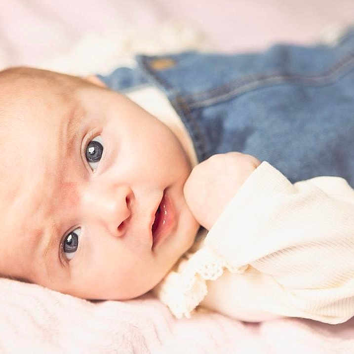 Yazmin is registered to the contest to win money with this photo: baby, blanket, child, closeup, clothing, cute, denim, expression, eyes, face, hand, indoor, infant, laying, newborn, overalls, person, portrait, skin, soft