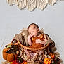 baby, newborn, sleeping, basket, orange_outfit, autumn, pumpkins, pinecones, fall_leaves, macrame, blanket, cozy, decor, wood_floor, soft_lighting, portrait, child, cute, resting, indoor