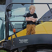 Oliver joined the competition — help win amazing prizes! child, boy, smiling, yellow_vehicle, tractor, agriculture, large_tire, outdoor, machinery, black_rail, clothing, short_sleeve_shirt, pants, blonde_hair, standing, daylight, farm_equipment, vehicle, happy, metal