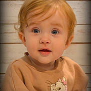 Ashlynn is registered to the contest to win money with this photo: baby, blond_hair, blue_eyes, cartoon, cat_design, child, close_up, clothing, curly_hair, face, indoor, looking_at_camera, open_mouth, portrait, smiling, surprised, sweater, toddler, wide_eyed, wooden_background