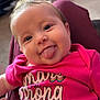 baby, infant, tongue_out, pink_shirt, text_on_clothing, happy, smiling, indoor, carpet, crib, furniture, person, portrait, cute, child, hair, clothing, closeup, face, playful