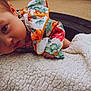 baby, child, face, curious, floral_clothing, blanket, texture, tire, outdoor, closeup, infant, cute, expression, skin, head, hand, person, photography, portrait, colorful