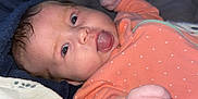 Ashlynn is registered to the contest to win money with this photo: baby, infant, face, tongue, hand, onesie, clothing, blanket, bed, sleepwear, cute, child, young, person, skin, expression, indoor, cozy, raised_fist, lying_down