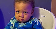 Messiah joined the competition — help win amazing prizes! toddler, child, high_chair, blue_clothing, indoor, serious_expression, dinosaur_pattern, person, baby, furniture, seat, young_child, pajamas, hands, face, curly_hair, sitting, expression, purple_lighting, home