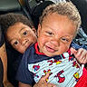 child, children, car_seat, smile, superhero_clothing, curly_hair, happy, cute, indoors, portrait, two_kids, sitting, family, candid, close_up, person, casual, red_clothing, blue_clothing, car_interior