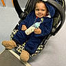 Messiah is registered to the contest to win money with this photo: baby, bottle, baby_carrier, blue_clothing, child, floor, footwear, fuzzy_slippers, indoor, infant, person, plush_clothing, seat, smile, toy, young_child, face, hand, head, cozy