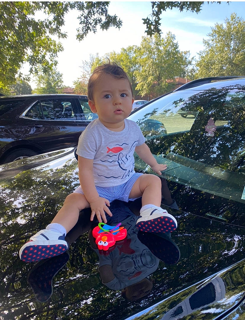 Alan joined the competition — help win amazing prizes! automotive_design, automotive_exterior, automotive_lighting, automotive_tire, bumper, car, grass, hood, motor_vehicle, person, plant, recreation, shorts, sky, t_shirt, tints_and_shades, toddler, tree, trunk, vehicle