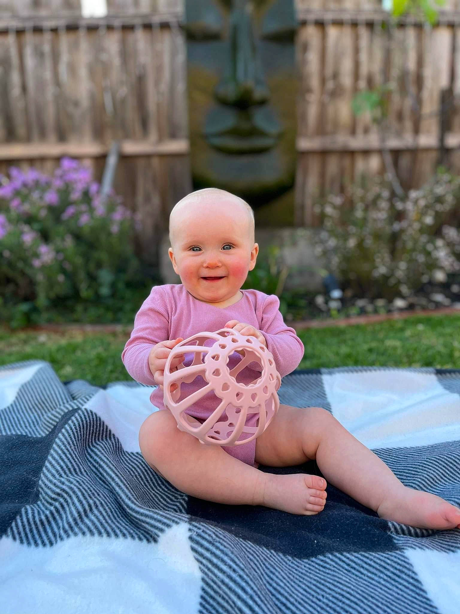 Maia is registered to the contest to win money with this photo: baby, baby_toddler_clothing, barefoot, child, fence, foot, fun, garden, grass, happy, head, human_leg, joy, leisure, pattern, person, plant, recreation, sandal, sitting