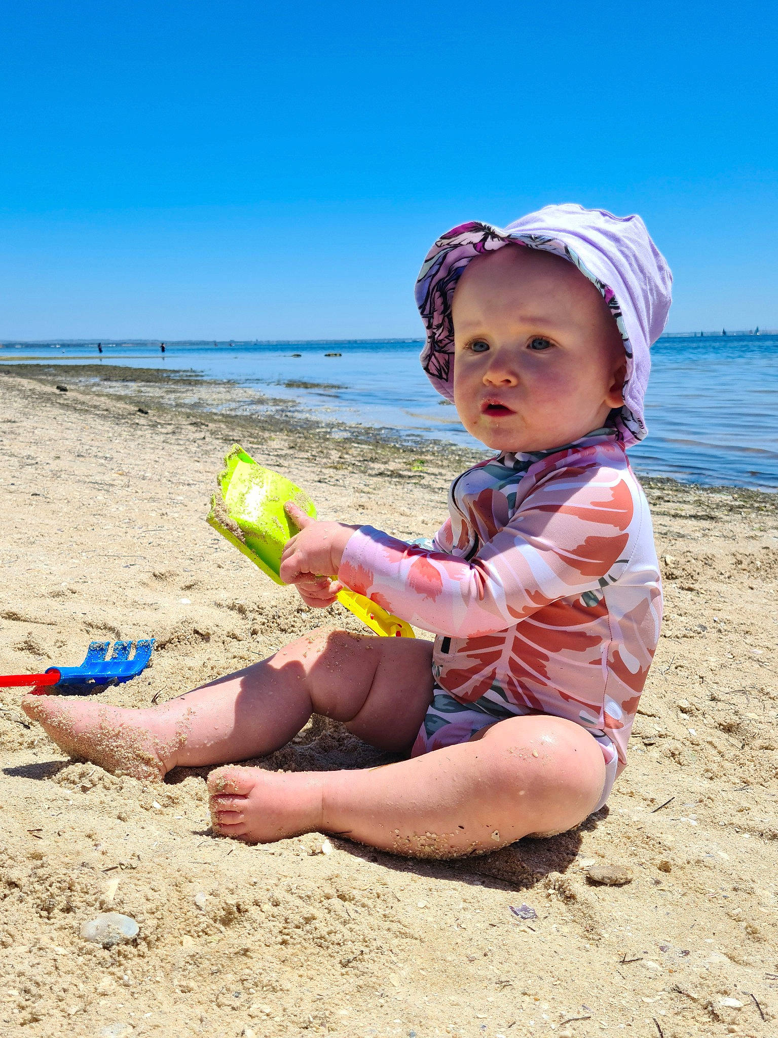 Maia is registered to the contest to win money with this photo: baby_toddler_clothing, beach, child, foot, fun, happy, hat, headwear, human_leg, knee, leisure, ocean, people_in_nature, person, sand, sitting, sky, sun_hat, thigh, toddler
