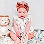 baby, child, headband, bow, dress, giraffe_print, plush_toy, lion, blanket, floral, sitting, hands, feet, cute, indoor, portrait, infant, wooden_plaque, holding, smiling