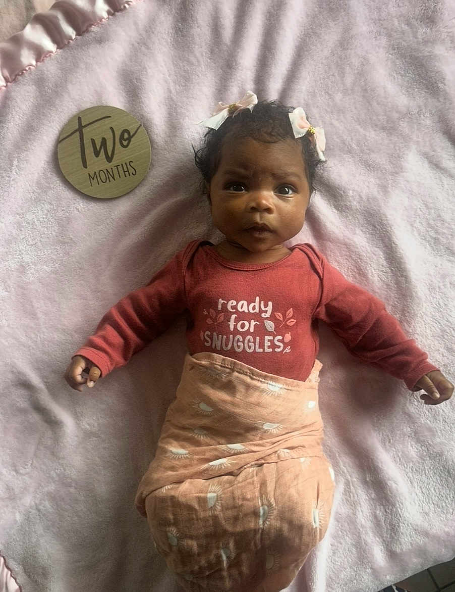 Clementine joined the competition — help win amazing prizes! baby, infant, blanket, pink, clothing, face, person, newborn, lying_down, cute, adorable, hair_bow, wooden_sign, text, bedroom, soft_texture, portrait, snuggles, two_months, expression