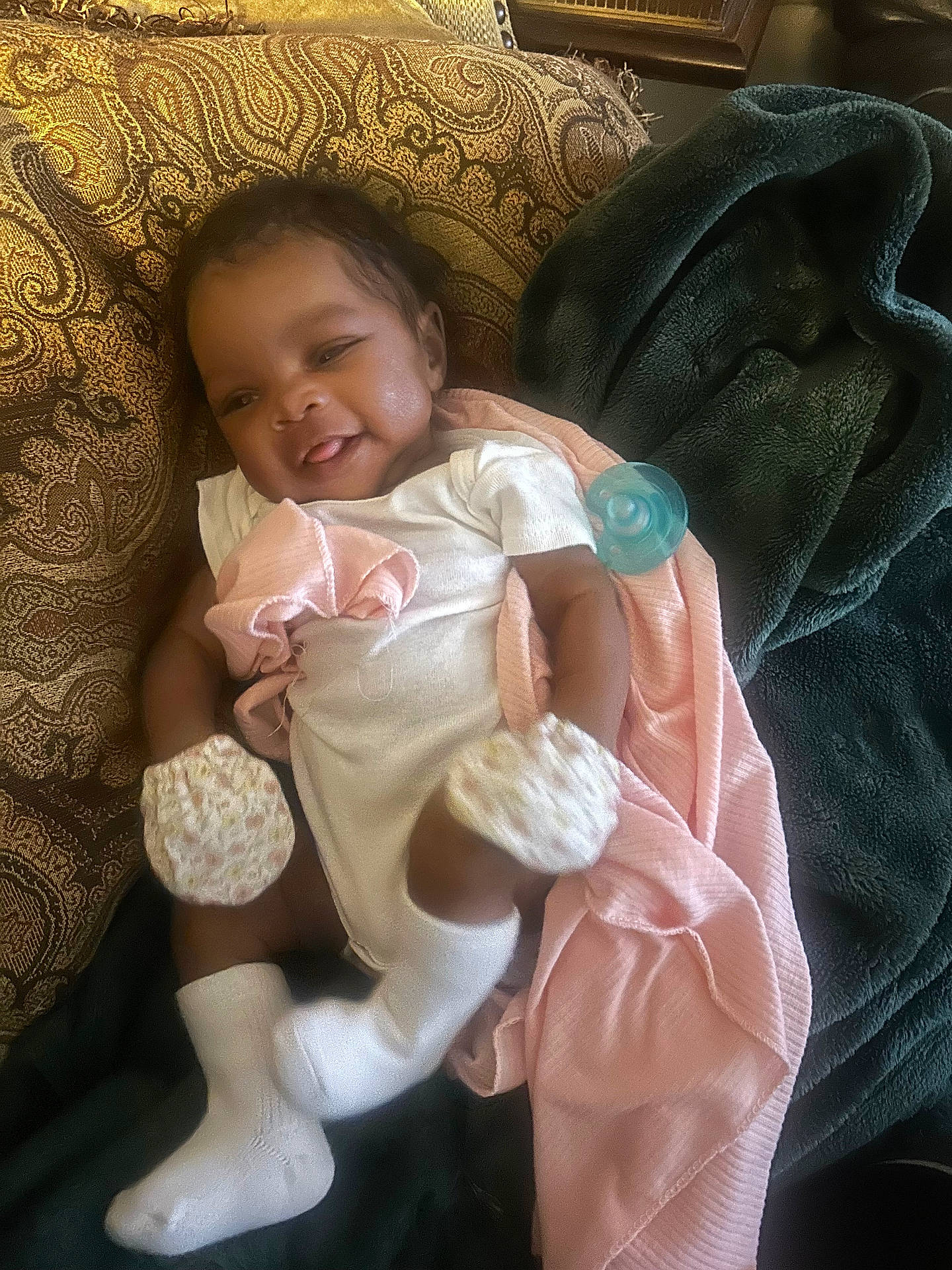 Clementine joined the competition — help win amazing prizes! baby, blanket, child, cozy, cushion, cute, green_blanket, indoor, infant, lying_down, mittens, pacifier, patterned_fabric, person, relaxed, smiling, socks, soft_fabric, tongue_out, white_clothing