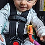 Jaxson is registered to the contest to win money with this photo: baby, child, car_seat, smiling, toy, pajamas, infant, safety_harness, cute, happy, face, person, seatbelt, colorful, small_toy, footwear, indoors, closeup, child_safety, playful