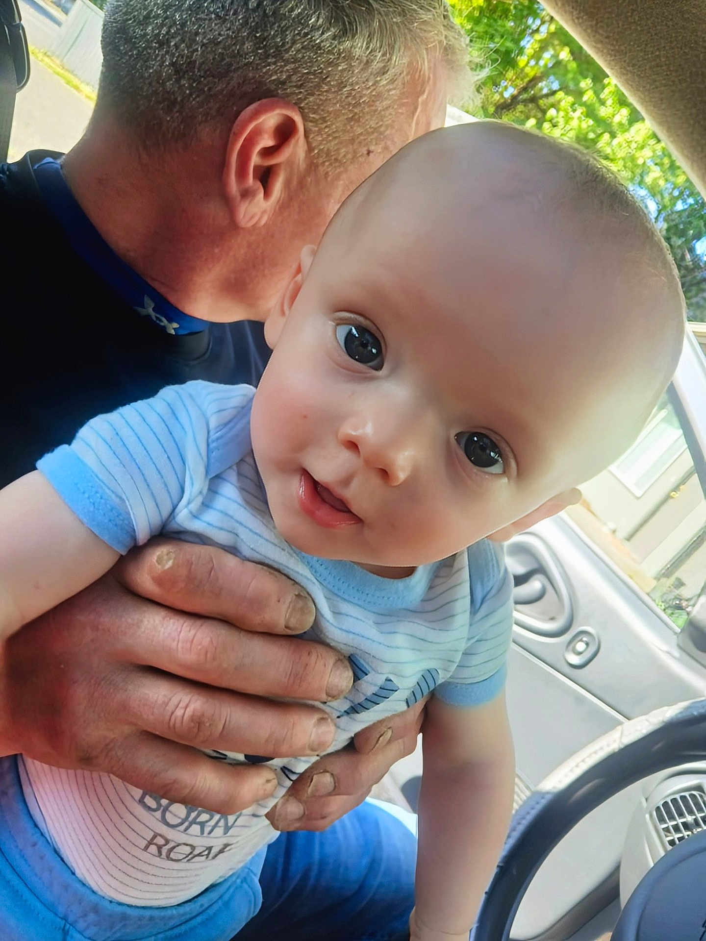 Jaxson is registered to the contest to win money with this photo: baby, child, adult, hand, car, vehicle_interior, window, person, face, skin, clothing, blue_shirt, striped_shirt, curious, holding, closeup, portrait, indoors, daylight, human