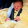 newborn, baby, sleeping, blanket, yellow_blanket, car_seat, black_straps, infant, cozy, soft_texture, child, peaceful, portrait, wrapped, cute, indoors, close_up, small_hands, resting, comfort