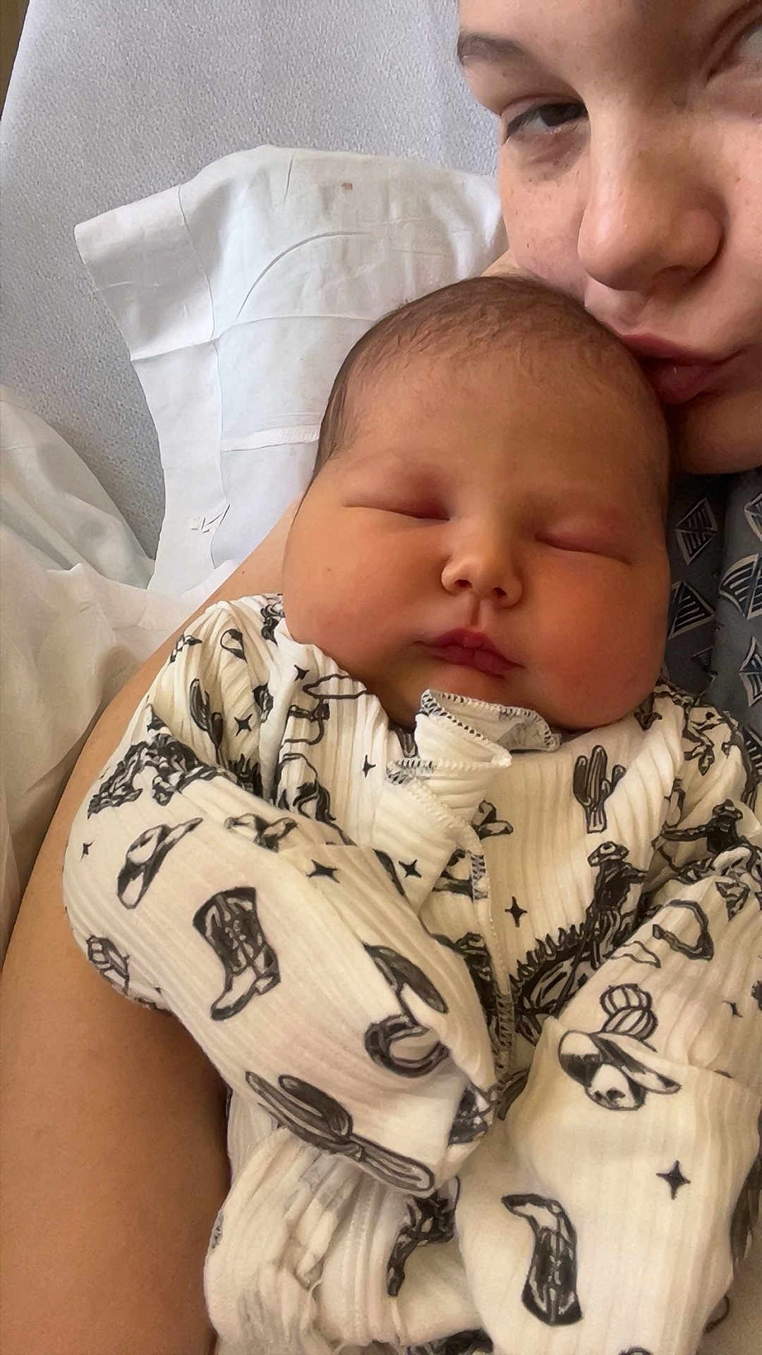 Lily joined the competition — help win amazing prizes! baby, newborn, infant, sleeping, parent, mother, kiss, swaddle, onesie, patterned_clothing, cowboy_hat_pattern, pillow, hospital_bed, closeup, portrait, arm, cheek, peaceful, soft_lighting, cuddle