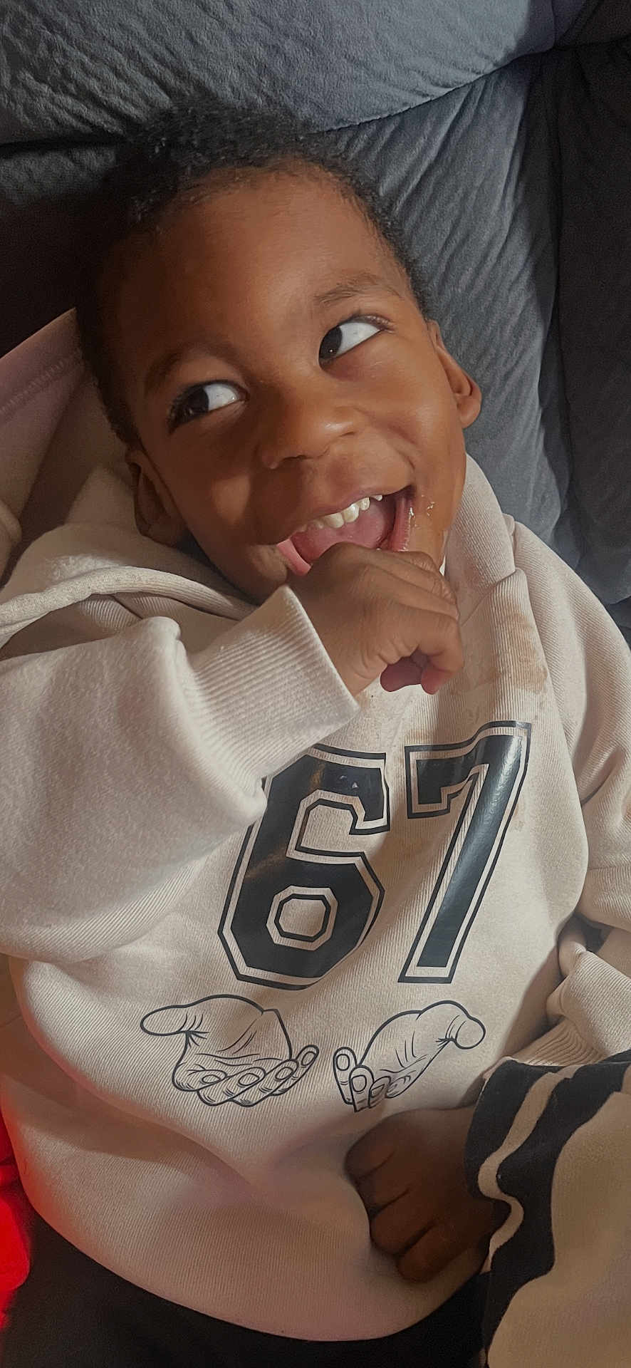 Champ is registered to the contest to win money with this photo: child, kid, portrait, smiling, playful, hoodie, number_67, hand_in_mouth, teeth, couch, pillow, closeup, indoor, candid, clothing, laugh, expressive_eyes, bedding, cozy, casual