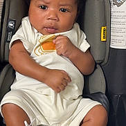 July joined the competition — help win amazing prizes! baby, infant, child, car_seat, car, portrait, sitting, looking_at_camera, curly_hair, brown_skin, white_outfit, sneakers, gold_shoes, indoors, vehicle, safety_labels, fashion, close_up, happy, photography
