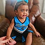 toddler, child, smiling, blue, black, cheerleading_outfit, hair_clips, hand_holding, leather_chair, indoor, happy, person, cute, baby, portrait, sitting, skin, furniture, young_child, expression