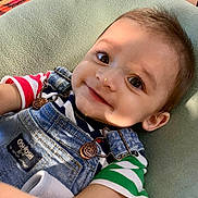 Sebastian joined the competition — help win amazing prizes! baby, child, smile, face, denim_overalls, striped_shirt, green, red, blue, cushion, closeup, portrait, cute, happy, infant, small, skin, eyes, hair, casual_clothing