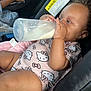 toddler, baby, milk_bottle, car_seat, hello_kitty, clothing, blanket, infant, cute, milk, feeding, child, seat, pink, hand, face, skin, curly_hair, indoor, person