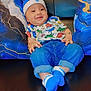 baby, blue_hat, blue_socks, casual, child, couch, cute, denim_pants, dinosaur_shirt, fashion, hand, happy, indoor, jewelry, leather, person, pillow, portrait, relaxed, smiling