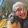 blanket, closeup, cozy, curtain, dog, face, furniture, glasses, hair, hand, happy, home, indoor, pet, plant, portrait, scarf, smiling, window, woman