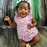 Jaliyah is registered to the contest to win money with this photo: baby, child, smile, dress, pink, bows, hair, cushion, blanket, striped, pattern, indoor, happy, person, infant, footwear, comfortable, cute, portrait, relaxed