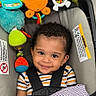 toddler, child, car_seat, toy, curly_hair, smile, striped_shirt, blanket, baby_toys, infant, cute, happy, indoors, seat_belt, colorful, playful, portrait, baby, child_safety, young_child