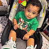 toddler, child, baby_seat, sneakers, green_shirt, curly_hair, toy, blanket, indoor, person, cute, young_child, footwear, car_seat, looking_up, casual_clothing, seated, expression, colorful, closeup