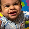 baby, child, smiling, onesie, indoor, colorful, playmat, flooring, wooden_floor, happy, cute, person, infant, face, portrait, young_child, home, sitting, patterned_clothing, playful