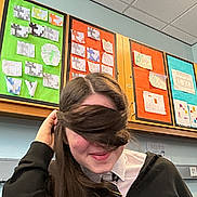 Jamel joined the competition — help win amazing prizes! child, student, classroom, hair_covering_face, smile, playful, school_uniform, tie, hand, bulletin_board, cabinets, ceiling_tiles, desk, wall, school_projects, person, portrait, indoor, young_person, education