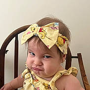 Skylar is registered to the contest to win money with this photo: toddler, child, grumpy_face, yellow_outfit, headband, cartoon_characters, wooden_chair, indoor, baby, expression, cute, person, sitting, portrait, funny_expression, clothing, hair, face, skin, background