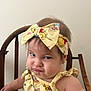 toddler, child, grumpy_face, yellow_outfit, headband, cartoon_characters, wooden_chair, indoor, baby, expression, cute, person, sitting, portrait, funny_expression, clothing, hair, face, skin, background