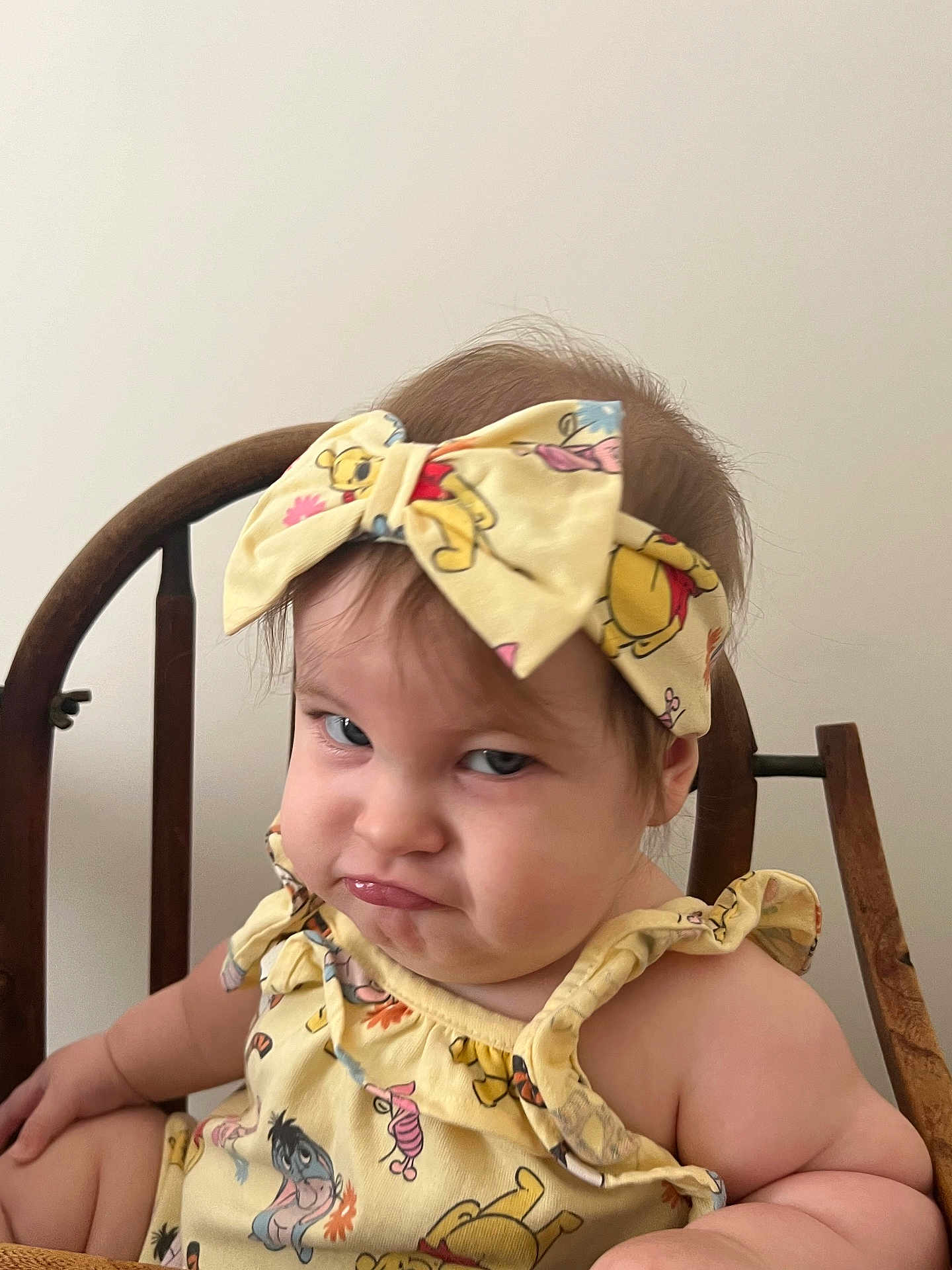 Skylar is registered to the contest to win money with this photo: toddler, child, grumpy_face, yellow_outfit, headband, cartoon_characters, wooden_chair, indoor, baby, expression, cute, person, sitting, portrait, funny_expression, clothing, hair, face, skin, background