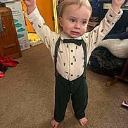 Phoenix is registered to the contest to win money with this photo: child, toddler, bow_tie, suspenders, shirt, pants, bare_feet, carpet, living_room, door, cardboard_box, clutter, smile, portrait, standing, cute, expression, indoor, clothing, young_child