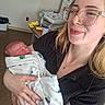 Elena is registered to the contest to win money with this photo: woman, newborn, baby, hospital_room, glasses, blanket, sleeping, holding, medical_equipment, person, indoor, portrait, happy, care, mother, child, hospital_bed, nurse_station, healthcare, tenderness