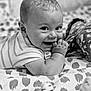 baby, infant, smiling, black_and_white, patterned_blanket, lying_down, cute, portrait, child, hand_in_mouth, soft_toys, close_up, happy, cheeks, striped_clothing, bed, indoors, candid, young_child, face