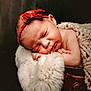 baby, newborn, sleeping, headband, red_bow, fur_blanket, knitted_blanket, wooden_surface, cozy, portrait, infant, peaceful, closeup, soft_light, indoors, cute, resting, child, warm, adorable