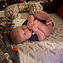 baby, infant, barefoot, mattress, blanket, indoor, cute, lying_down, foot_in_mouth, nursing_pillow, patterned_fabric, child, small_person, home, soft_lighting, skin, person, relaxed, toddler, cozy