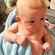 Reggie is registered to the contest to win money with this photo: baby, infant, blue_towel, diaper, skin, arm, hand, face, eyes, ear, indoor, fist, expression, curious, person, child, newborn, blanket, closeup, soft