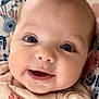 baby, infant, face, smile, eyes, close_up, child, cute, expression, skin, mouth, clothing, floral_pattern, cushion, portrait, young, happy, cheeks, person, indoors